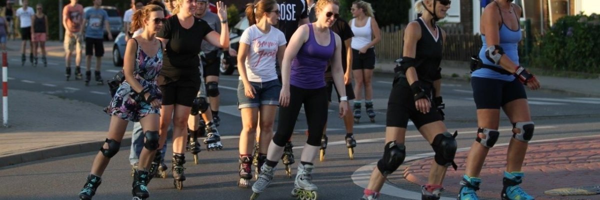 Auf dem Bild ist eine Gruppe Inline-Skatern zu sehen. Diese fährt bei der Abenddämmerung über einen Kreisverkehr.