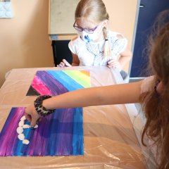 Zwei Mädchen erstellen ein Bild mit Muscheln und bunten Farben.