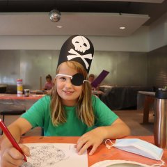 Ein Mädchen, das als Piratin verkleidet ist, malt ein Bild.