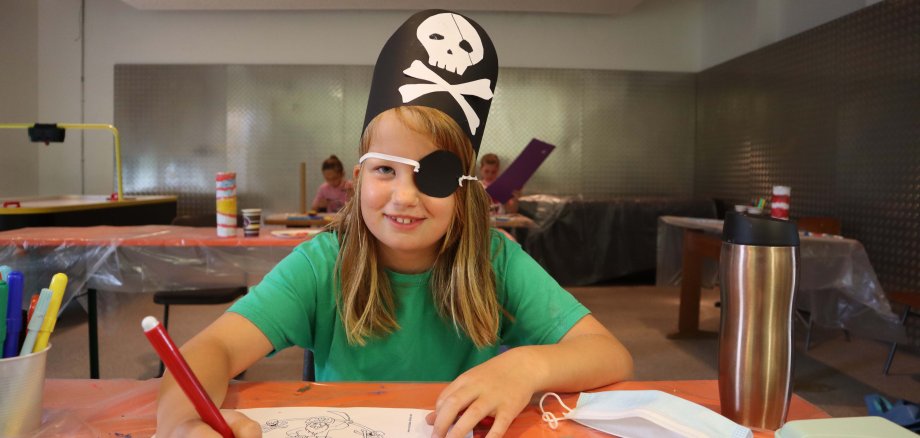 Ein Mädchen, das als Piratin verkleidet ist, malt ein Bild.