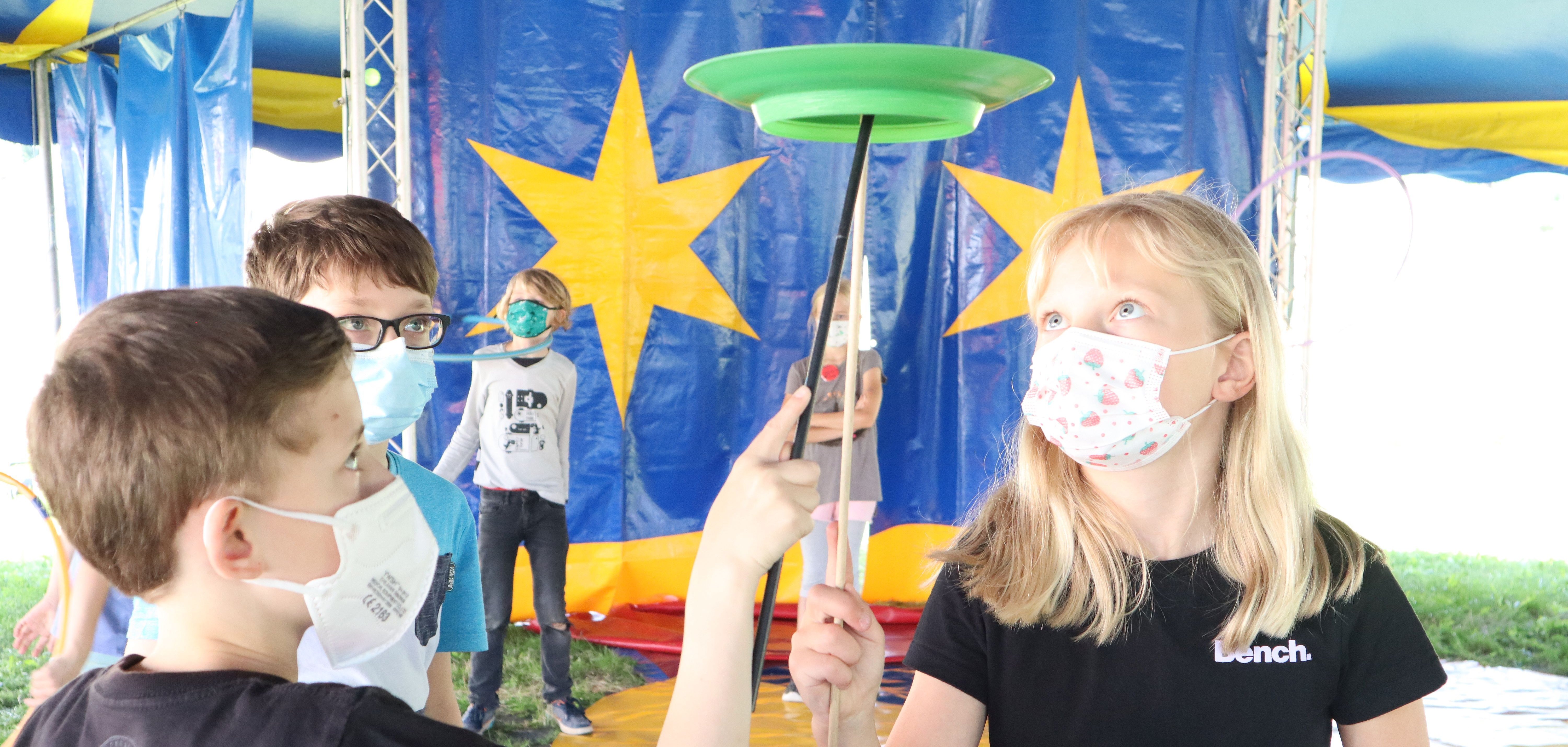 Auf dem Bild sieht man mehrere Kinder die probieren einen Zirkusteller auf einem Holzstarb zu Balenzieren 