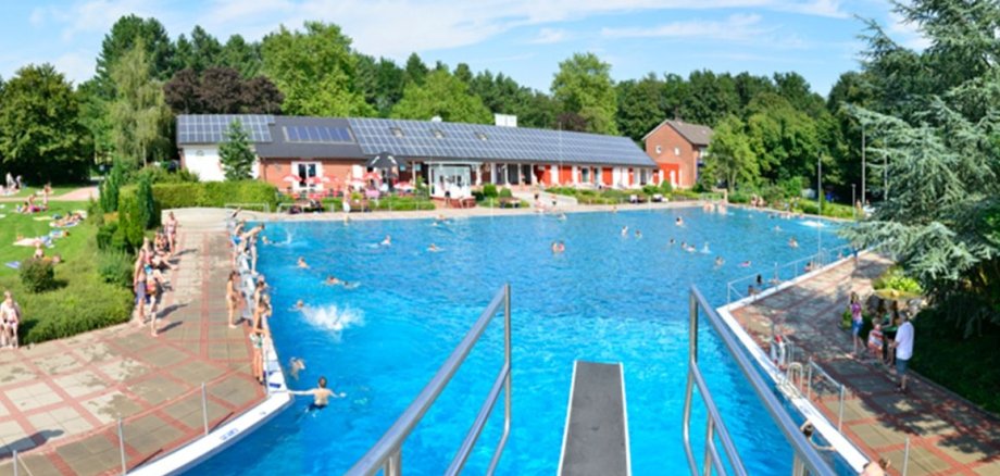 Überblick über das Eper Freibad mit einer Aufnahme des großen Schwimmbeckens in dem vereinzelnd Leute schwimmen. Im Hintergrund sieht man die Begrünung des Freibads.