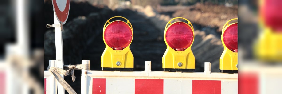 Rot weiß gestreifte Absperrplanke mit drei Warnlichtern auf der Absperrplanke