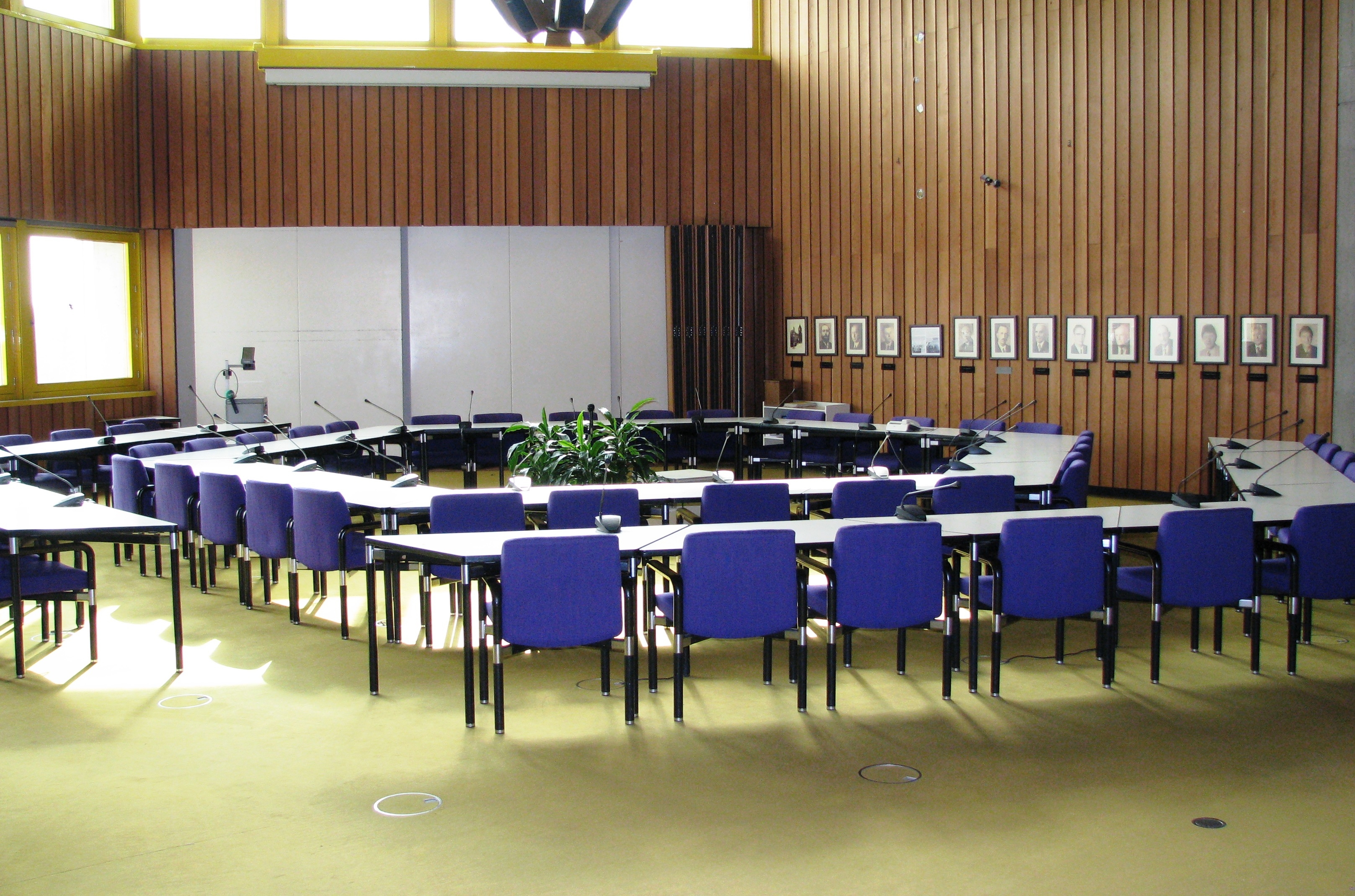 Der Sitzungssaal mit Tischen, Stühlen und einer Leinwand.