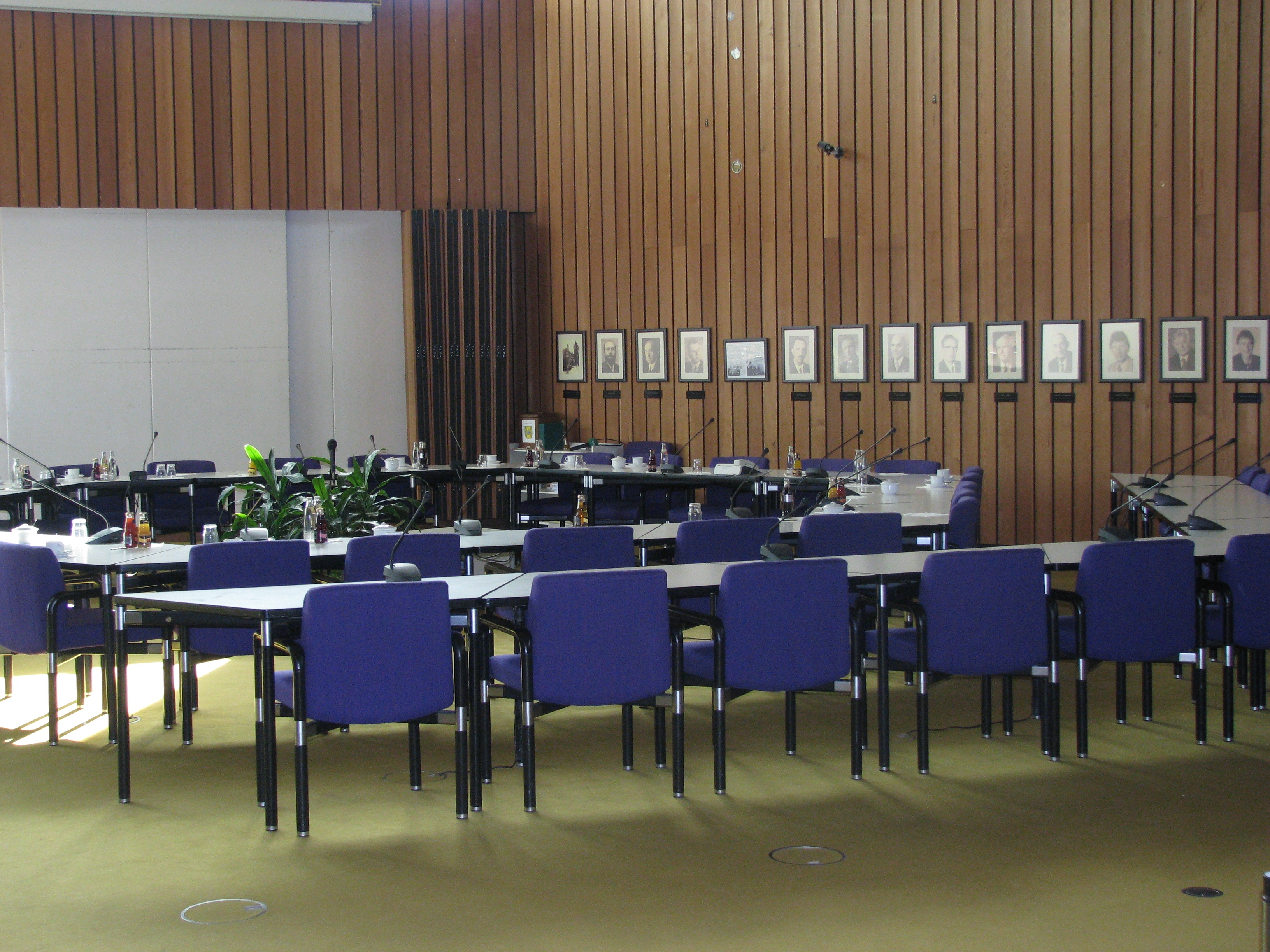 Der Sitzungssaal mit Tischen, Stühlen und einer Leinwand.