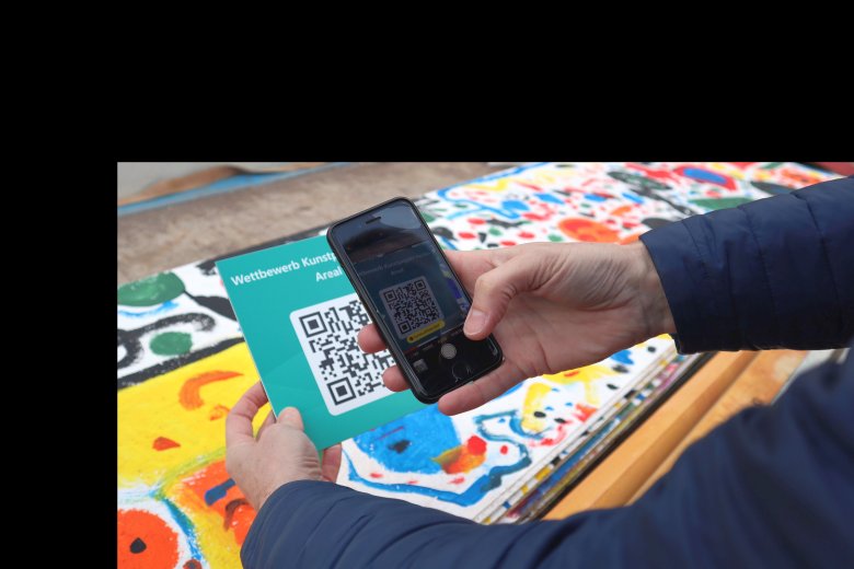 Man sieht den Bürgermeister, der einen QR-Code für einen Kunstwettbewerb scannt