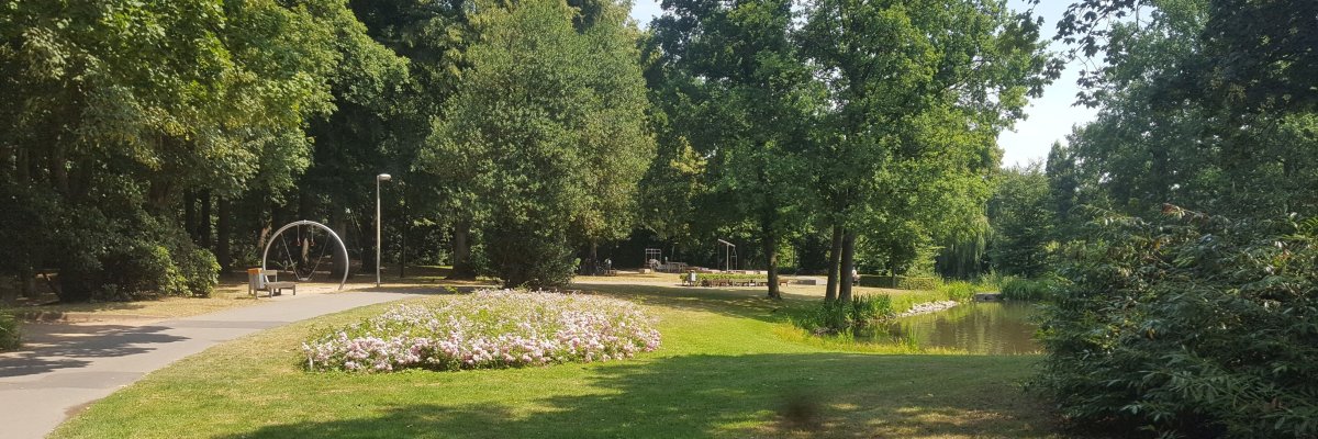 Blick in den Stadtpark vom kleinen Kinderspielplatz aus. Sichtbar ist ein Teil des Sees und ein Teil des großen Spielplatzes. Aufnahme aus dem Sommer mit entsprechender Begrünung.