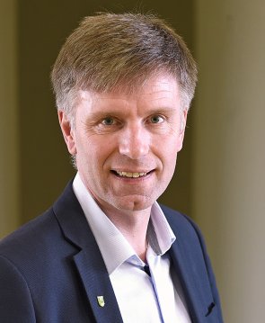 Der Bürgermeister Rainer Doetkotte ab Schulterhöhe. Er trägt ein dunkelblaues Sakko und ein weißes Hemd. Er steht leicht seitlich und lacht zähnezeigend in die Kamera.