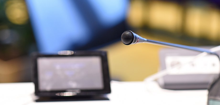 Ein Mikrofon und ein kleiner Bildschirm auf einem Tisch im Sitzungssaal.