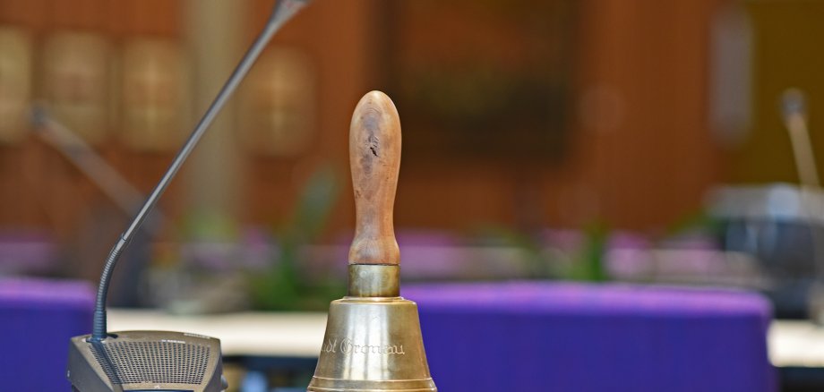 Ein Mikrofon und eine Klingel auf einem Tisch im Sitzungssaal.