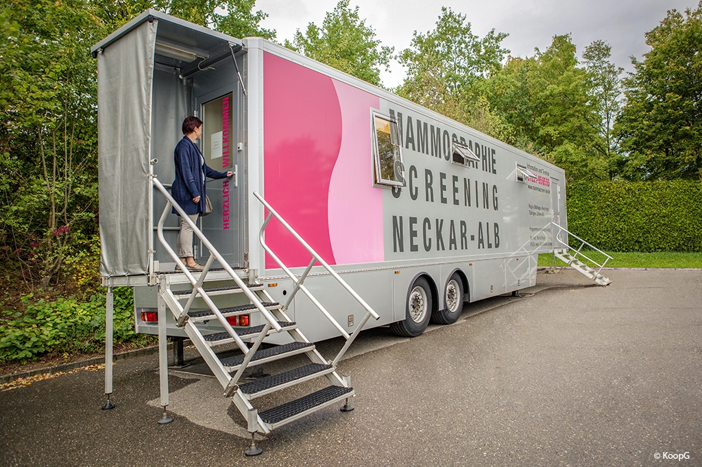 Eine Frau steht oben an der Treppe des Mammobils und öffnet die Tür.