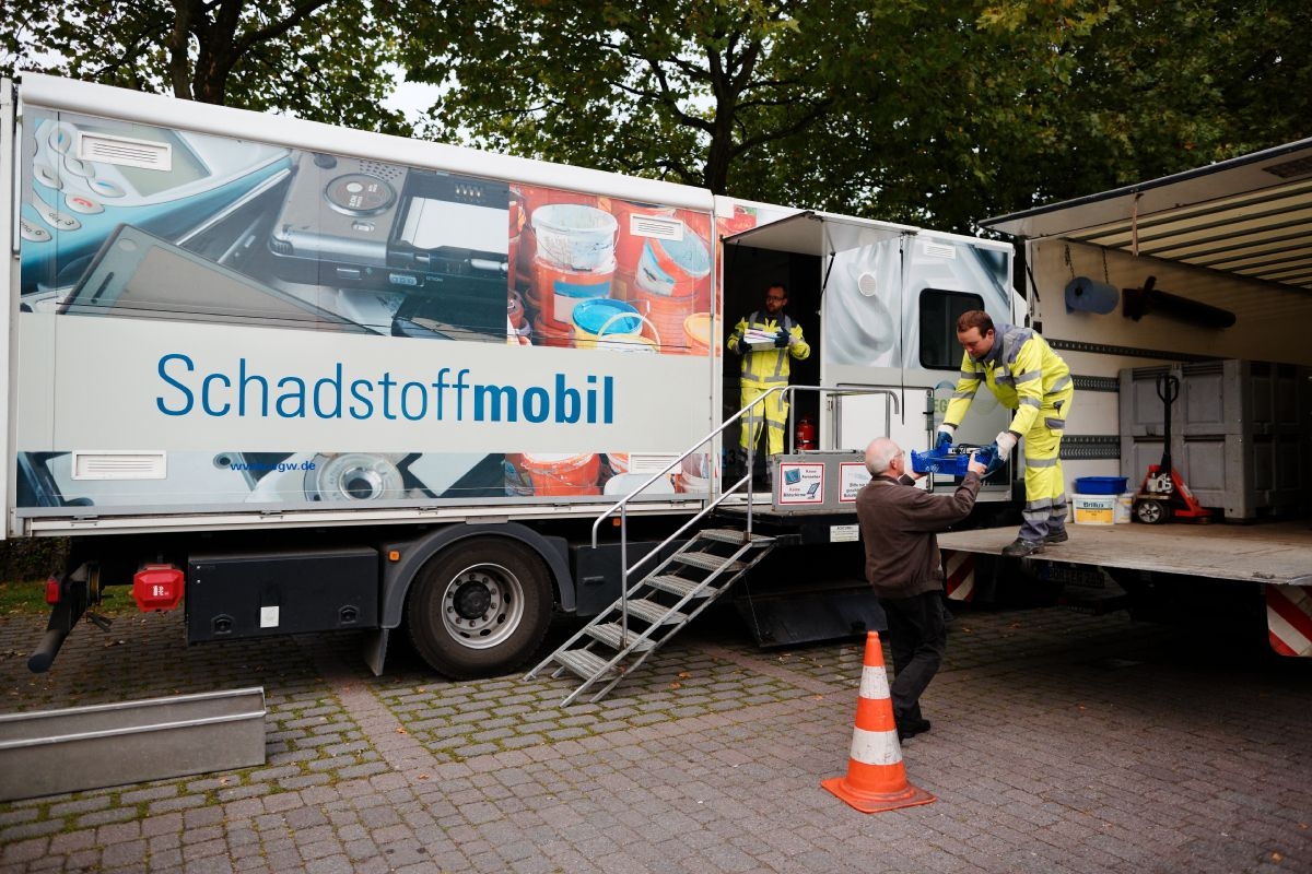 Zwei Mitarbeiter nehmen am Schadstoffmobil Müll von einem Mann entgegen.