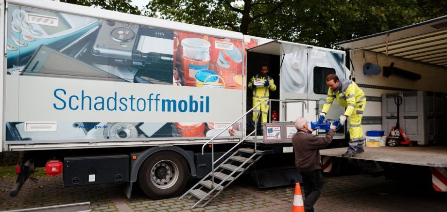 Zwei Mitarbeiter nehmen am Schadstoffmobil Müll von einem Mann entgegen.