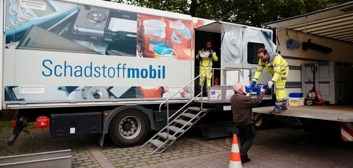 Zwei Mitarbeiter nehmen am Schadstoffmobil Müll von einem Mann entgegen.