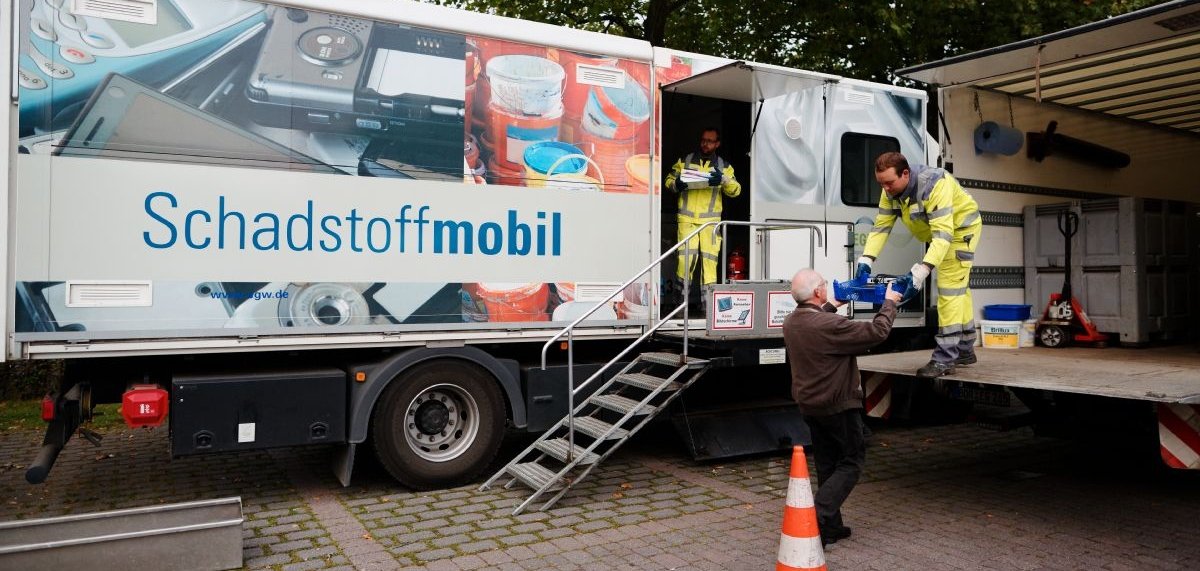 Zwei Mitarbeiter nehmen am Schadstoffmobil Müll von einem Mann entgegen.