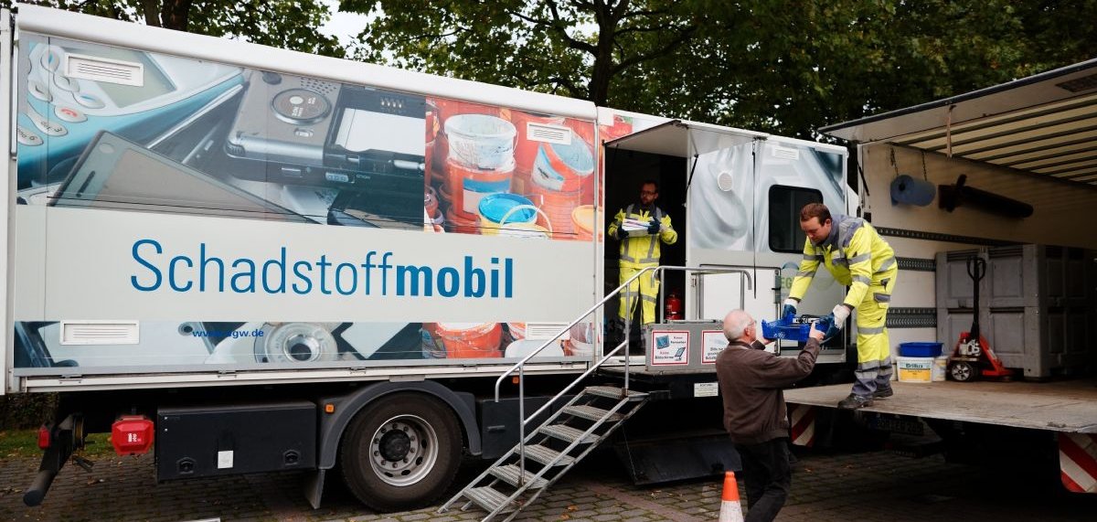 Zwei Mitarbeiter nehmen am Schadstoffmobil Müll von einem Mann entgegen.