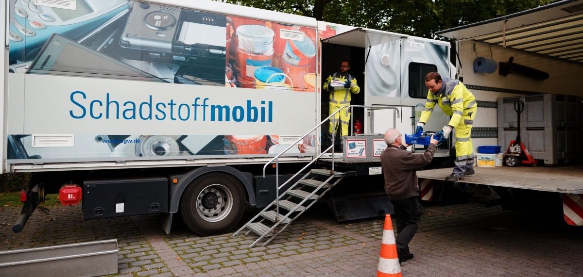 Zwei Mitarbeiter nehmen am Schadstoffmobil Müll von einem Mann entgegen.