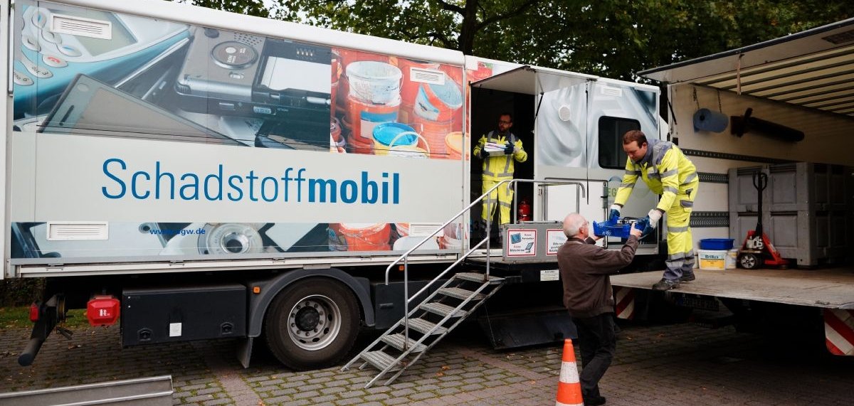 Zwei Mitarbeiter nehmen am Schadstoffmobil Müll von einem Mann entgegen.