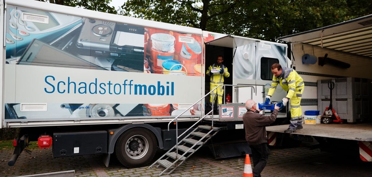 Zwei Mitarbeiter nehmen am Schadstoffmobil Müll von einem Mann entgegen.