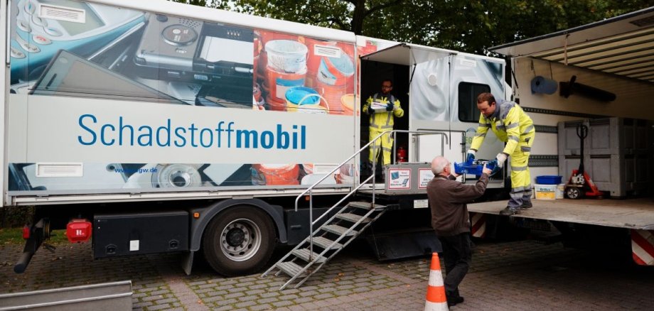 Zwei Mitarbeiter nehmen am Schadstoffmobil Müll von einem Mann entgegen.