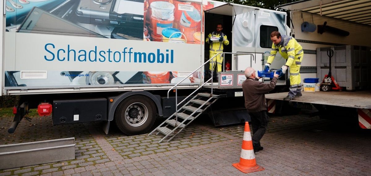 Zwei Mitarbeiter nehmen am Schadstoffmobil Müll von einem Mann entgegen.