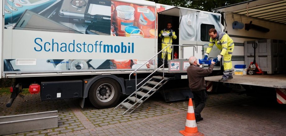 Zwei Mitarbeiter nehmen am Schadstoffmobil Müll von einem Mann entgegen.