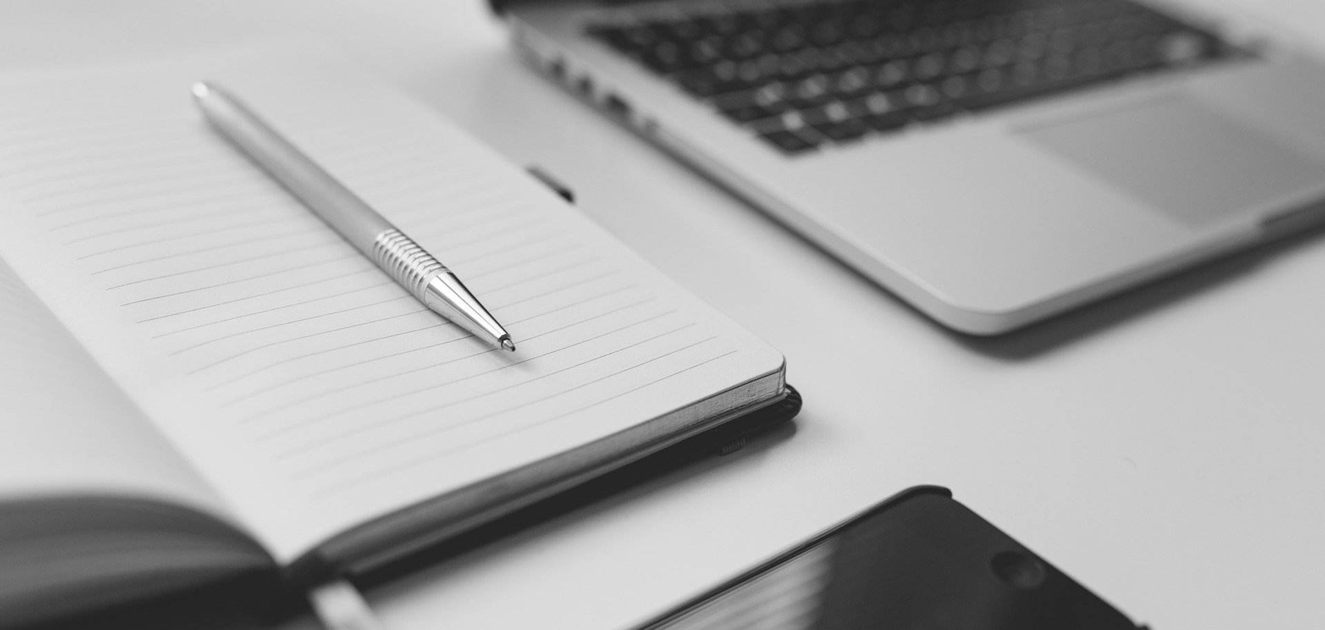 Vor einem Laptop liegen ein Smartphone und ein Notizbuch.