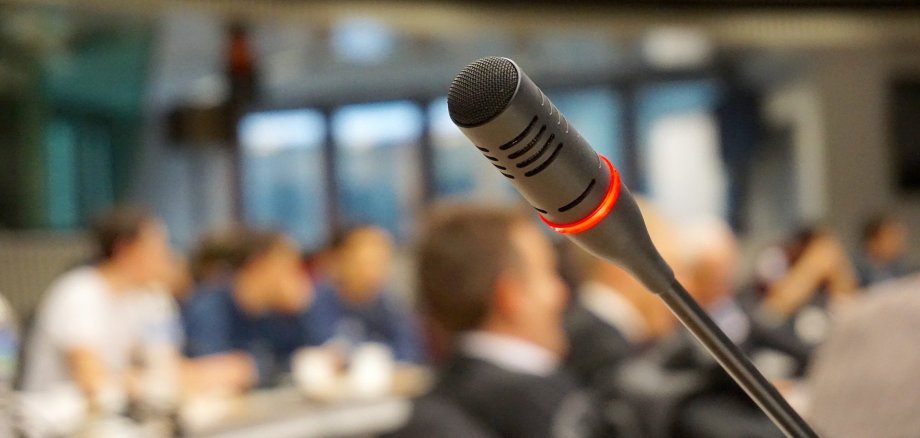 Ein Mikrofon in einem vollen Sitzungssaal.