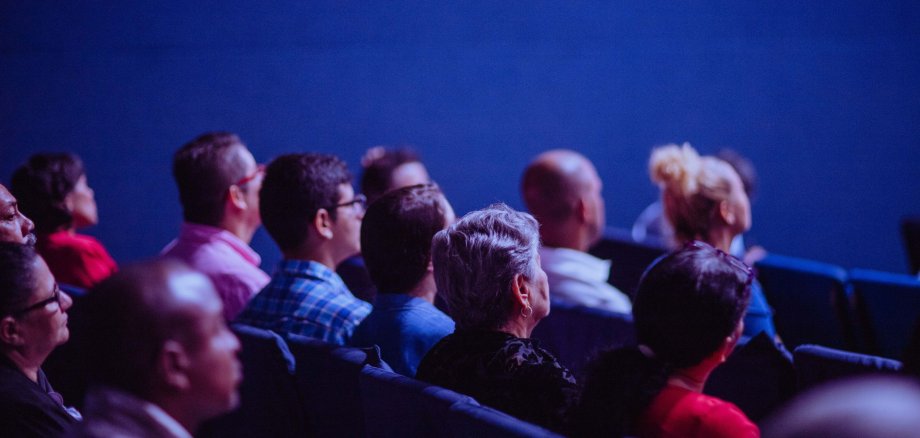 Eine Gruppe von Personen sitzt in einem Saal und hört einem Vortrag zu.