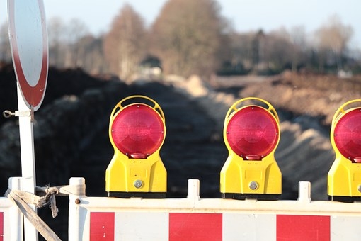 Baustelle Man sieht eine Baustellenabsperrung mit roten Lichtern vor einer Straße.