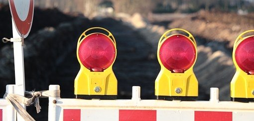 Man sieht eine Baustellenabsperrung mit roten Lichtern vor einer Straße.