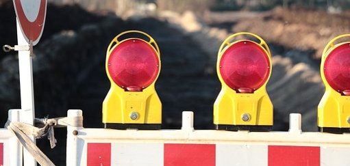 Man sieht eine Baustellenabsperrung mit roten Lichtern vor einer Straße.