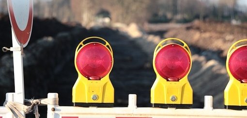 Man sieht eine Baustellenabsperrung mit roten Lichtern vor einer Straße.
