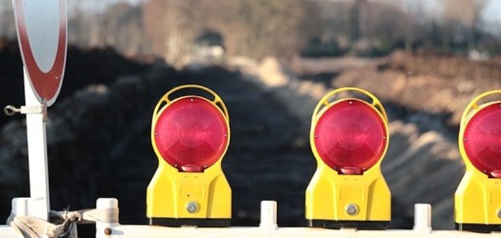 Man sieht eine Baustellenabsperrung mit roten Lichtern vor einer Straße.