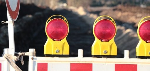 Man sieht eine Baustellenabsperrung mit roten Lichtern vor einer Straße.