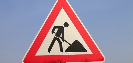 Man sieht ein rotweißes Baustellenschild mit einem schwarzen Männchen mit Schüppe und Sandhaufen.