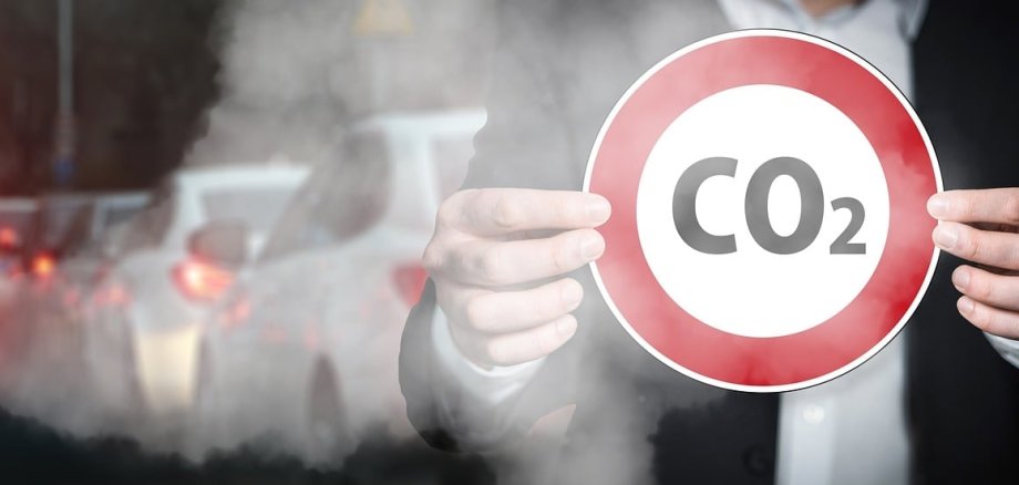 Symbolisch wird ein Warnschild mit der Aufschrift CO2 vor einigen PKW gehalten Symbolisch wird ein Warnschild mit der Aufschrift CO2 vor einigen PKW gehalten