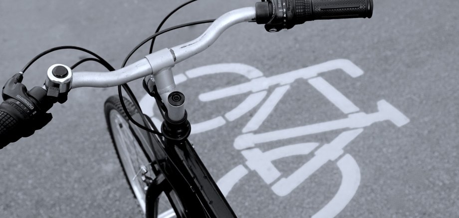 Lenker eines Fahrrads aus der Vogelperspektive. Unter dem Lenker sieht man ein weißes Fahrradsymbol, das auf den grauen Asphalt gedruckt wurde.