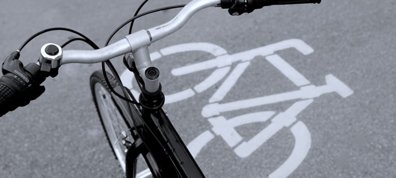 Lenker eines Fahrrads aus der Vogelperspektive. Unter dem Lenker sieht man ein weißes Fahrradsymbol, das auf den grauen Asphalt gedruckt wurde.