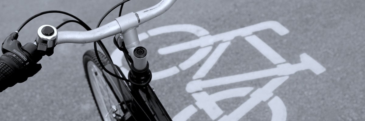Lenker eines Fahrrads aus der Vogelperspektive. Unter dem Lenker sieht man ein weißes Fahrradsymbol, das auf den grauen Asphalt gedruckt wurde.