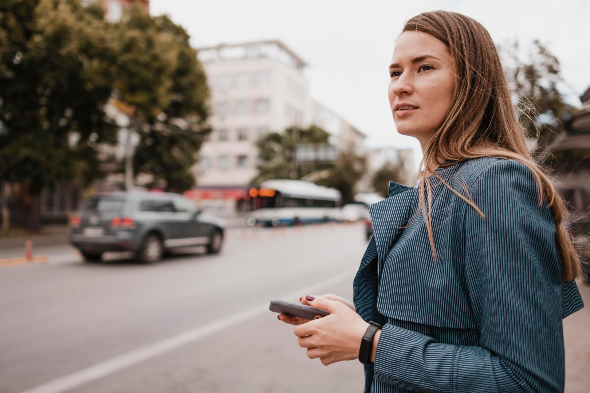 Eine Frau mit einem Handy in der Hand schaut auf die Straße. 