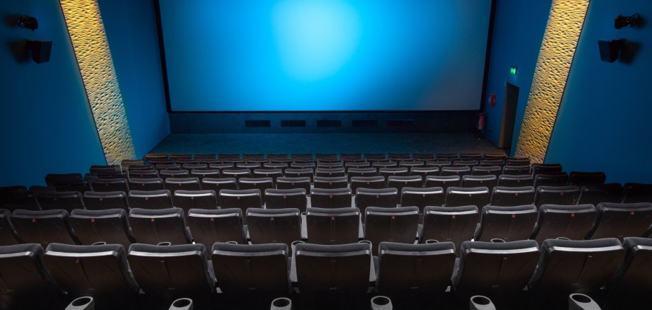 Leerer Kinosaal mit vielen Sitzen und einer großen blauen Leinwand, auf der kein Film spielt.
