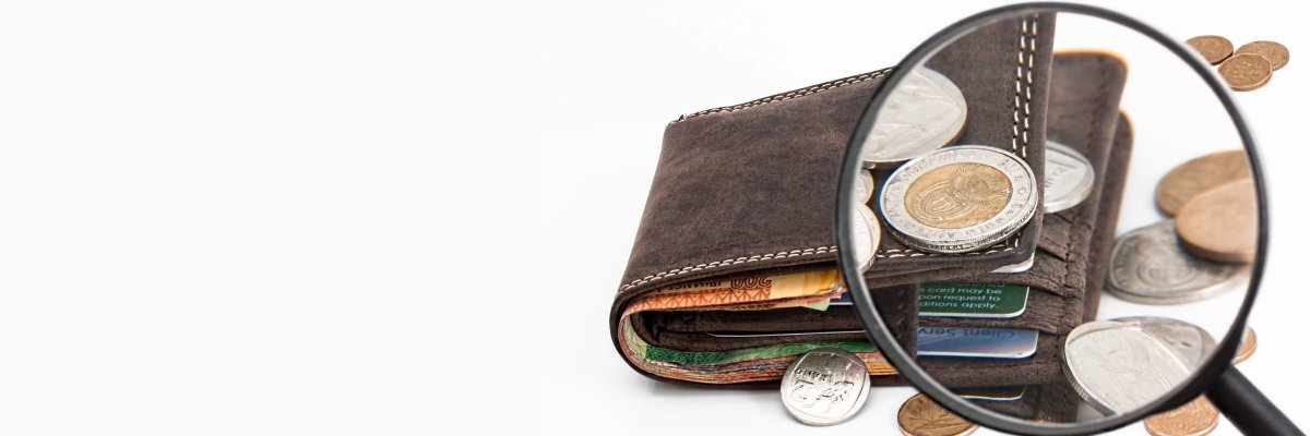 Der Betrachter des Fotos schaut durch eine Lupe auf ein braunes Lederportemonnaie, aus dem einige Euromünzen herausgefallen sind.