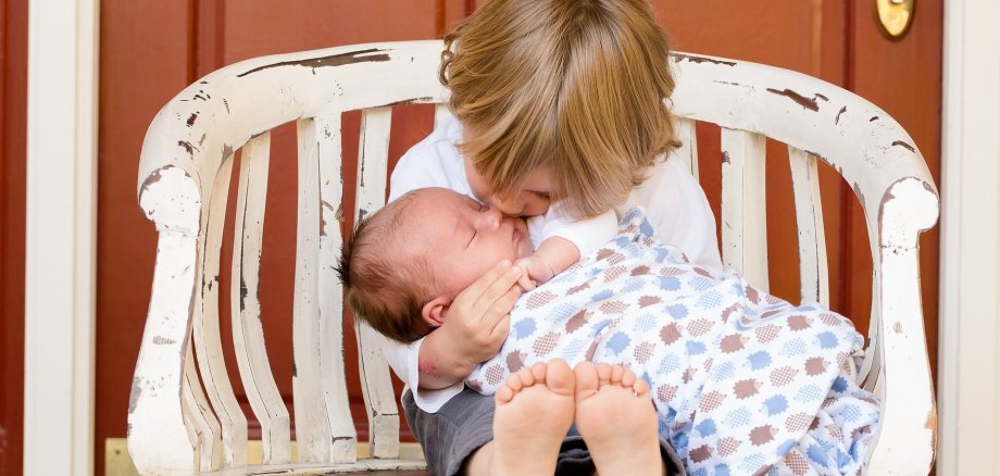 Ein Kleinkind hält ein Baby im Arm.