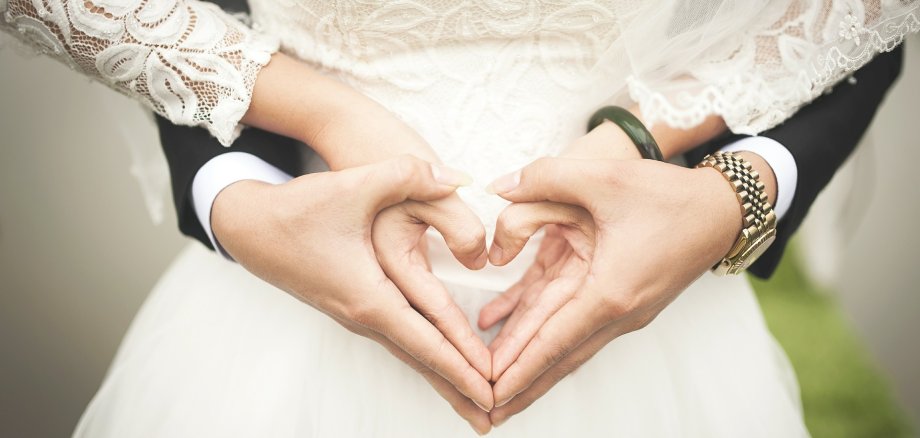 Die Hände von Braut und Bräutigam, die zusammen ein Herz formen.