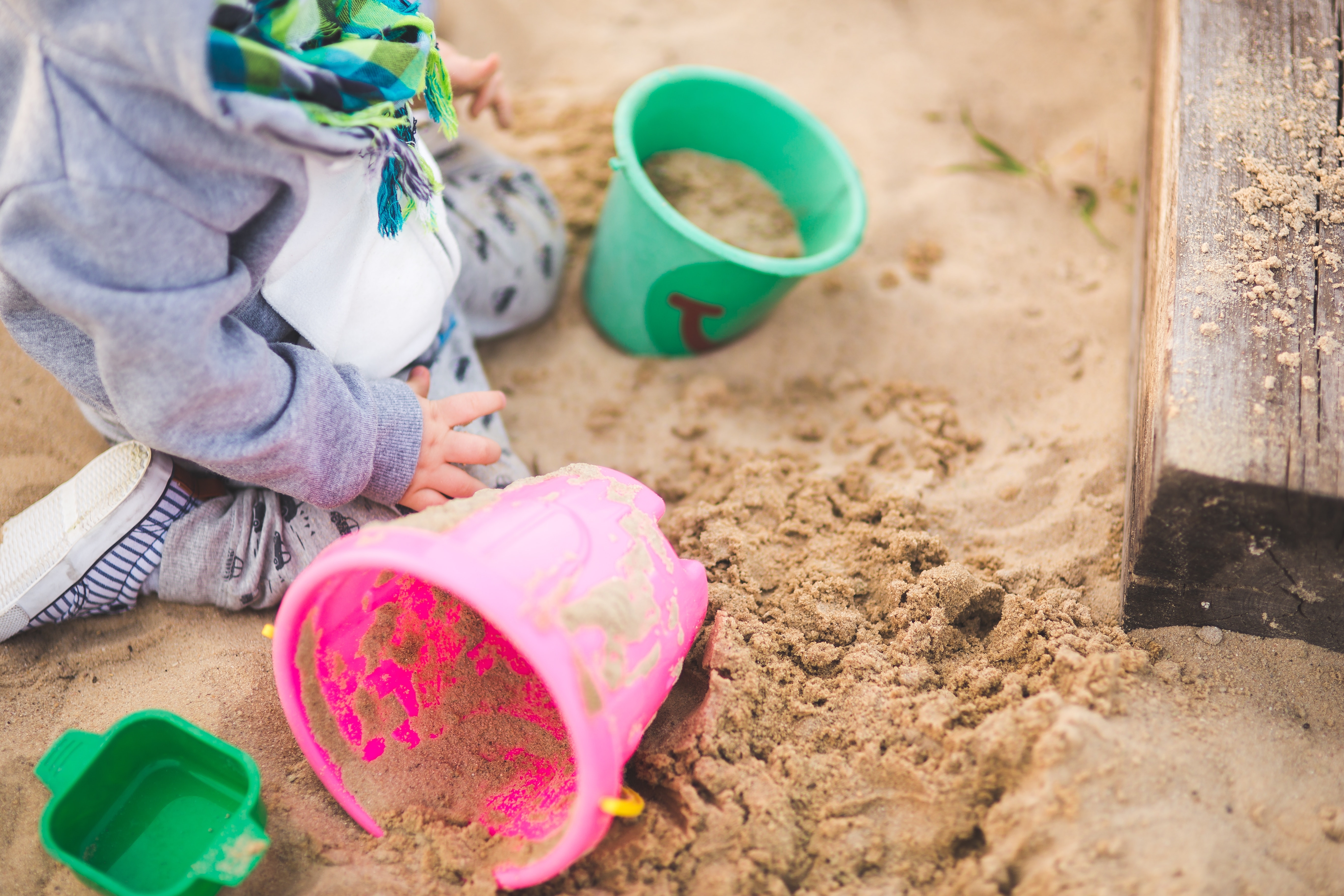 Ein Kind sitzt mit Spielsachen in einer Sandkiste.