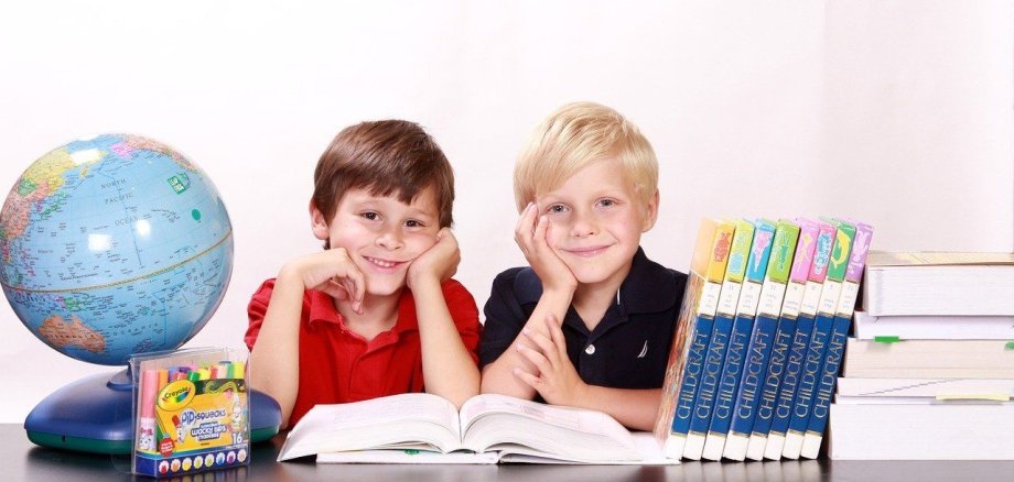 Zwei Schulkinder sitzen vor einem Globus und Büchern an einem Tisch.