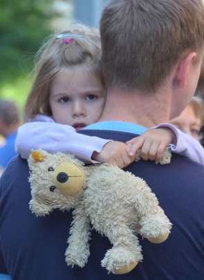 Kind mit Teddy und Vater Ein Kind ist auf dem Arm seines Vaters und hält einen Teddy in der Hand.