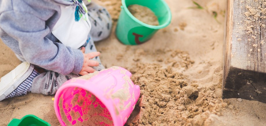 Ein Kind sitzt mit Spielsachen in einer Sandkiste.