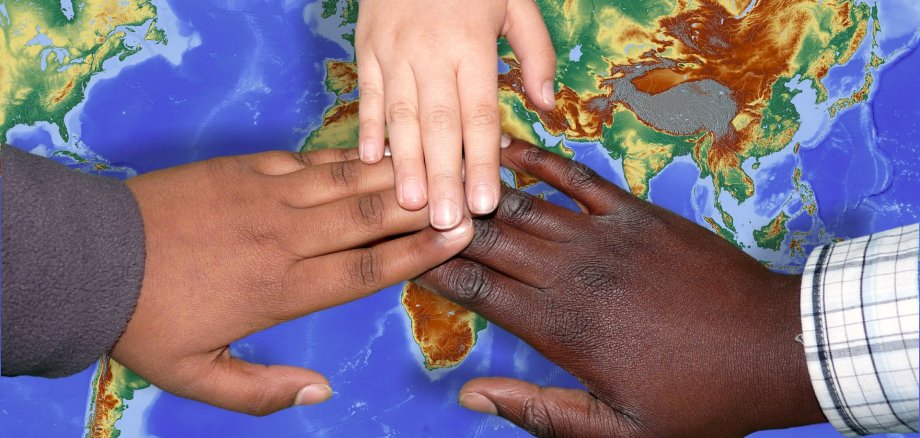 Drei Hände in unterschiedlen Hautfarben werden über die Weltkarte gehalten.